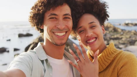 portrait of african american couple smiling and showing their ring on the rocks near the sea