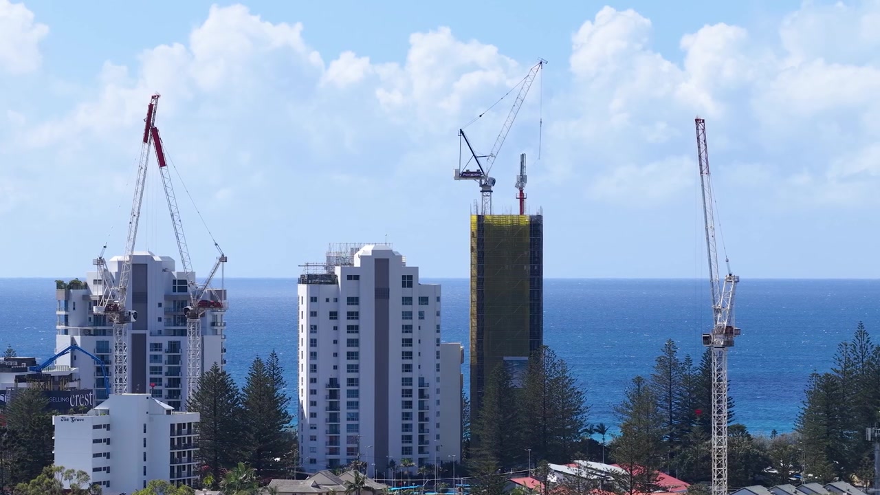 Static wide shot of skyscrapers and construction cranes against a blue ocean and sky