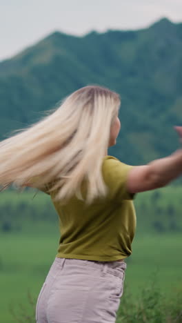 attractive smiling woman hiker with loose hair spins around against green mountain valley at wild eco preserve on gloomy day slow motion