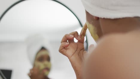 Happy-african-american-woman-apply-beauty-mask-on-face-in-bathroom