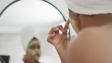 feliz mujer afroamericana aplica una máscara de belleza en la cara en el baño