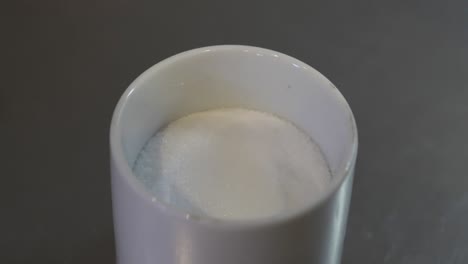 above angle slow motion shot of a tablespoonful of salt taken out of container in a kitchen.
