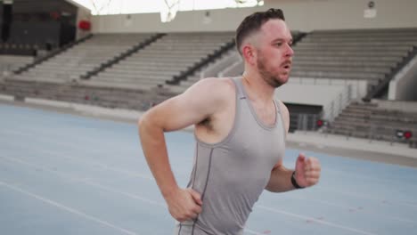 tired caucasian male athlete training, running at sports stadium