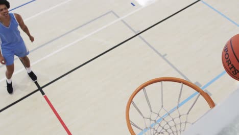 High-angle-of-diverse-male-basketball-team-training-at-indoor-court-and-scoring-basket,-slow-motion