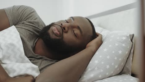 african man sleeping in bed in morning. unhappy male person hating morning.