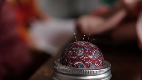 close-up of a seamstress putting a pin into a pincushion