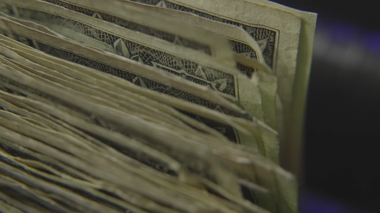 Extreme close-up of worn dollar bills flipping through a counting machine, capturing raw texture and movement in high detail.