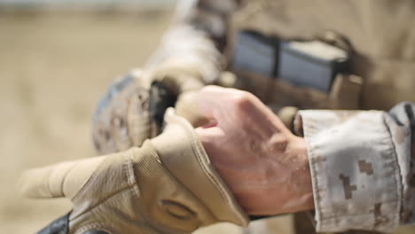 slow motion: a us marine positioned in the desert puts a tactical glove on his left hand