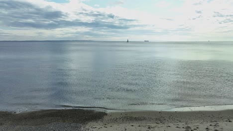 Weites-Meer-Und-Entferntes-Segelboot-Vom-Strand-In-Aarhus-Dänemark-Aus-Gesehen---Vorwärtsbewegende-Luftaufnahme-In-Der-Nähe-Des-Strandes