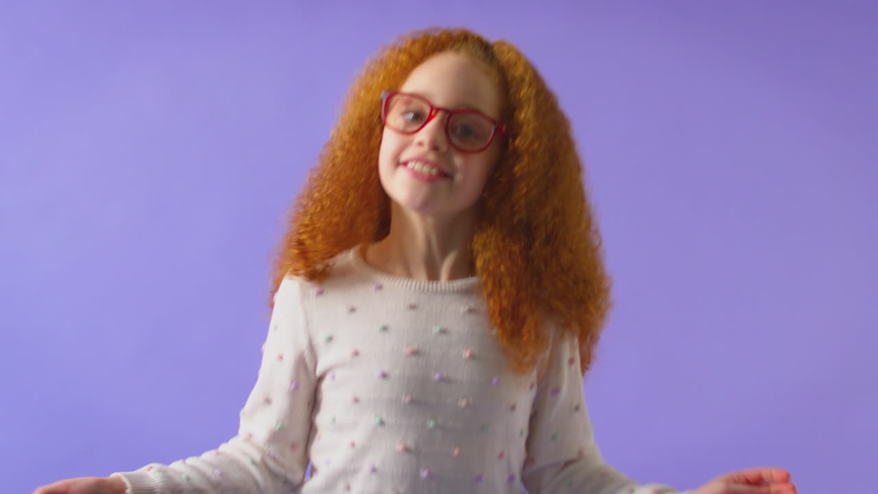 빨간 안경을 입은 활기찬 소녀가 보라색 배경에서 점프하고 춤을 추는 스튜디오  ⁇