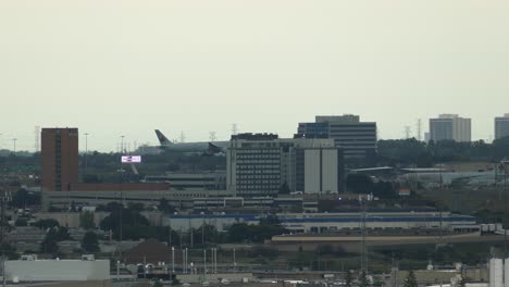 epic tracking shot of flying air canada plane between skyline buildings of toronto and runway of airport in background.