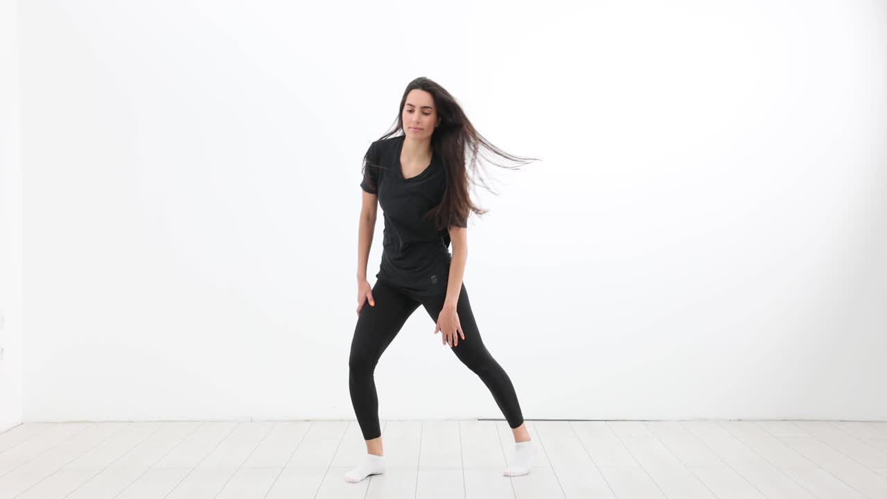 Kvinde i sort danser kraftfuldt, mens hendes lange hår svinger i et studie.