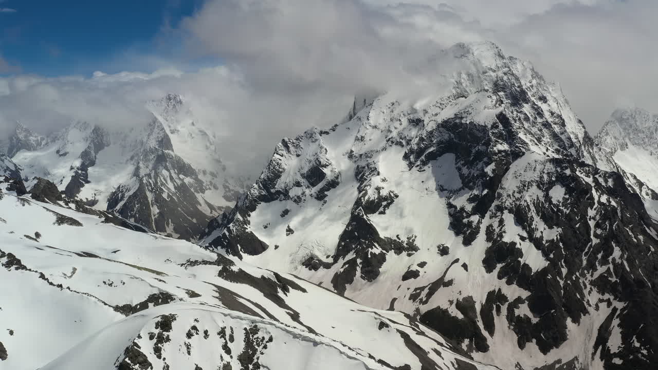 Volo aereo tra le nuvole di montagna sopra splendide vette innevate e ghiacciai.