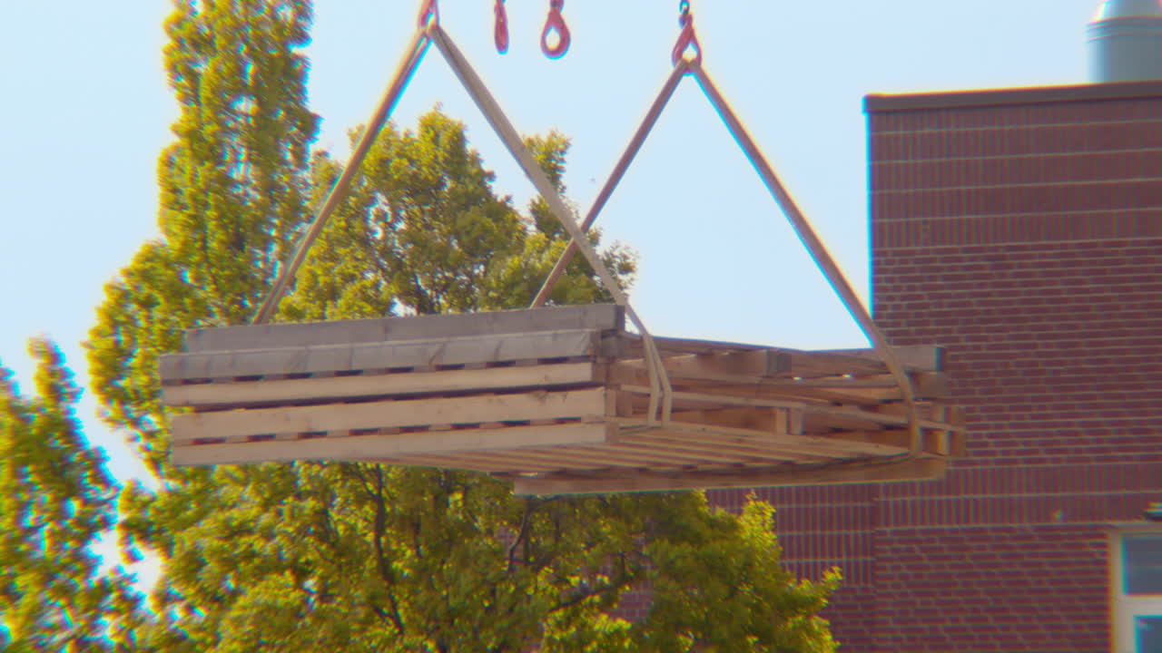 cierre de una grúa levantando y moviendo lentamente piezas de construcción de bloques de construcción de madera contrachapada para un proyecto de construcción con cuerdas y cadenas de derecha a izquierda en el marco en un día de primavera