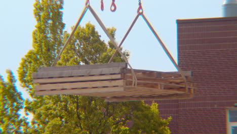 cierre de una grúa levantando y moviendo lentamente piezas de construcción de bloques de construcción de madera contrachapada para un proyecto de construcción con cuerdas y cadenas de derecha a izquierda en el marco en un día de primavera