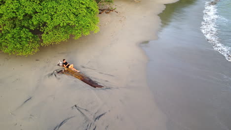 vista aérea de una turista relajándose en un tronco de árbol de madera en una playa desierta en manuel antonio, costa rica