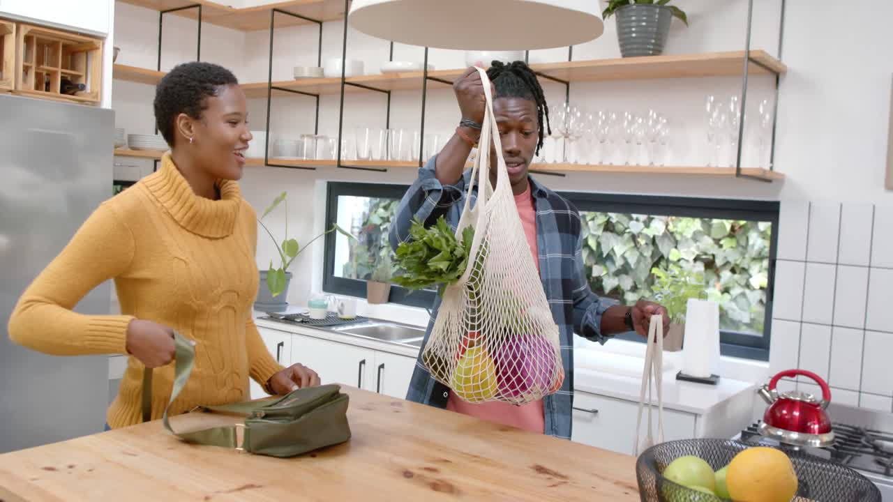 Happy african american couple unpacking groceries in kitchen, slow motion