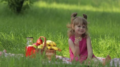 weekend at picnic. caucasian child girl on grass meadow with basket full of fruits. eating pancakes