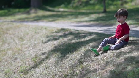 Un-Niño-Pequeño-Está-Sentado-En-Un-Campo-Verde-Bajo-Una-Luz-Moteada-Y-Tirando-Piedras