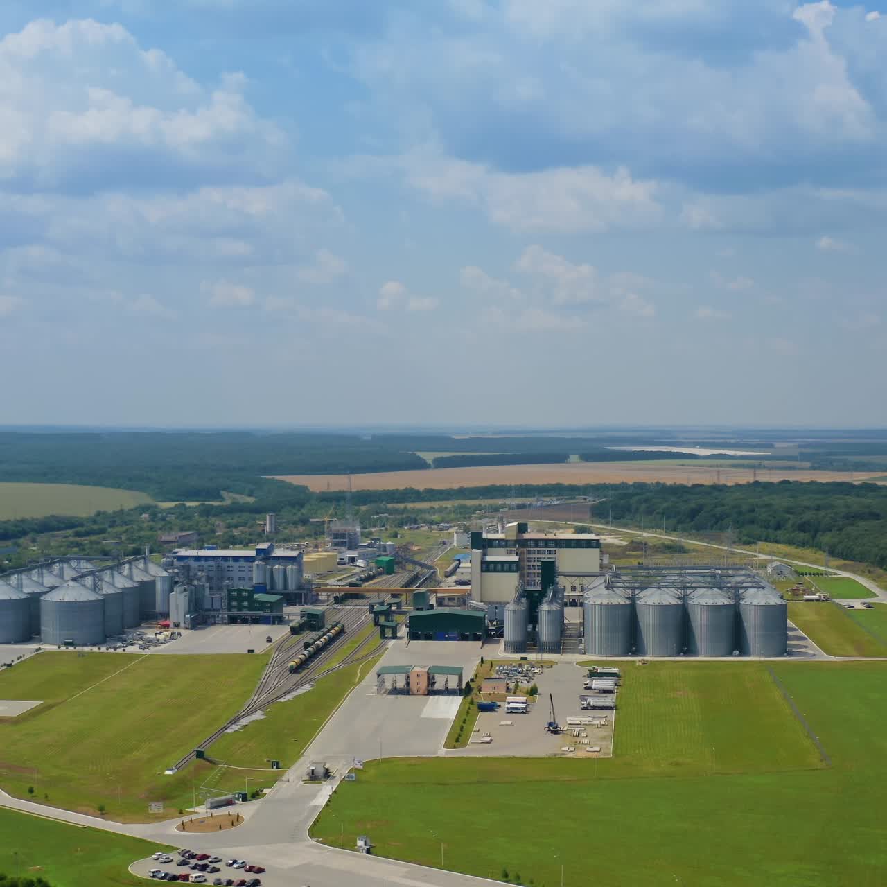 Large industrial plant among green nature. Modern factory with silos on field. Grain elevators in the countryside. Aerial view