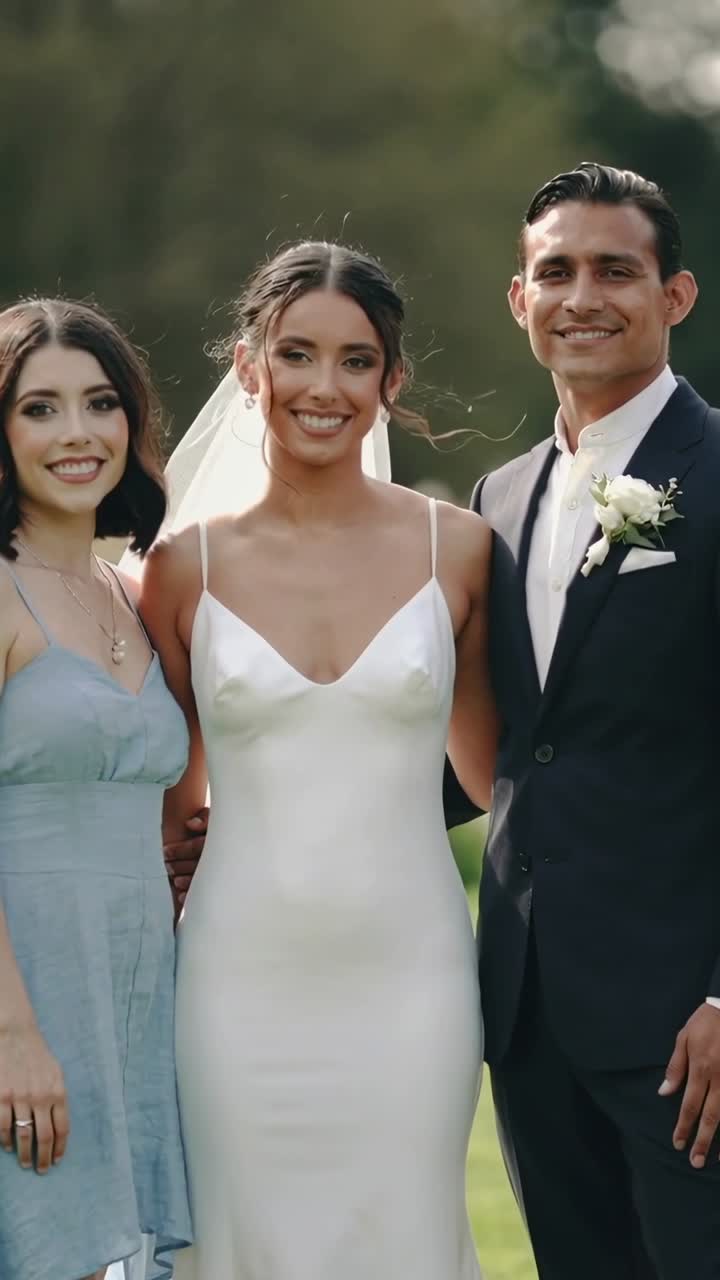 Video verticale: La telecamera inquadra sposa, sposo e damigella che posano in giardino per un ritratto di matrimonio, con velo, abito da sposa e completo.