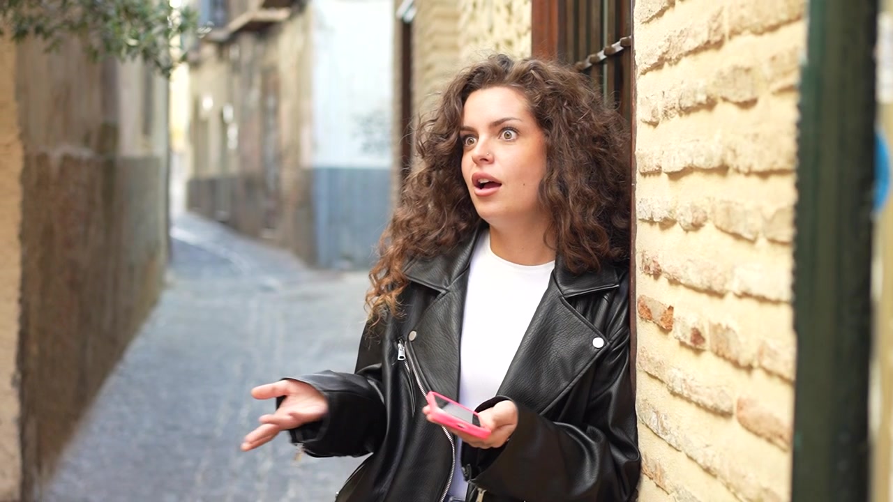 Una joven disfrutando de su smartphone mientras está de pie en un callejón encantador y pintoresco.
