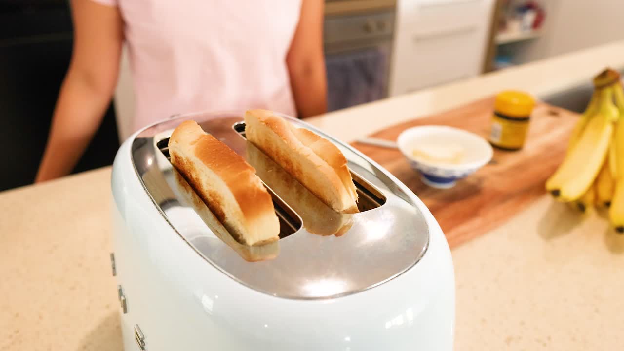 Slices of bread pop from a toaster on a kitchen counter with bananas and a jar nearby