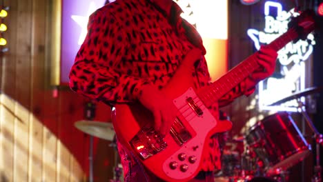 Male-guitarist-plays-electric-bass-guitar-on-stage-in-band,-red-lighting-slow-motion-4K