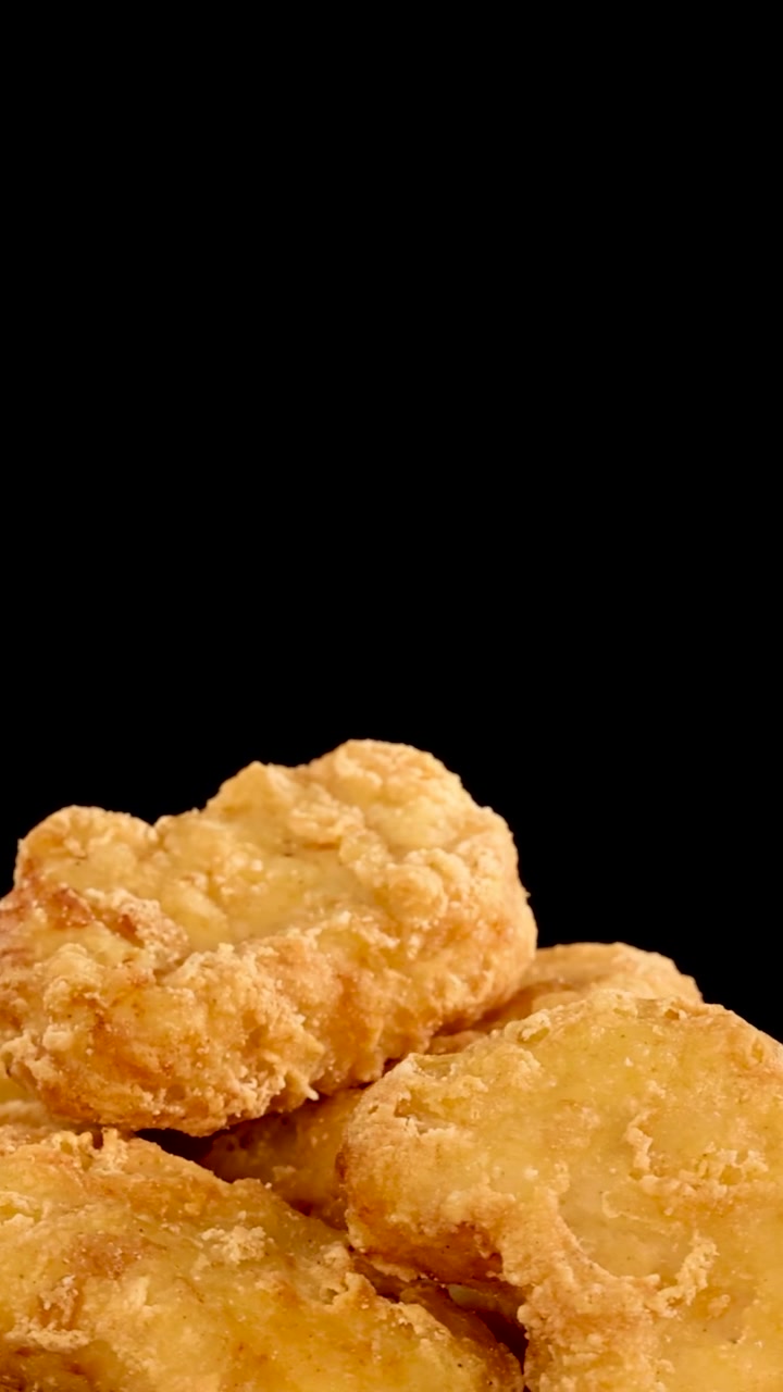 Una pila de nuggets de pollo empanados de color dorado gira suavemente sobre un fondo oscuro.