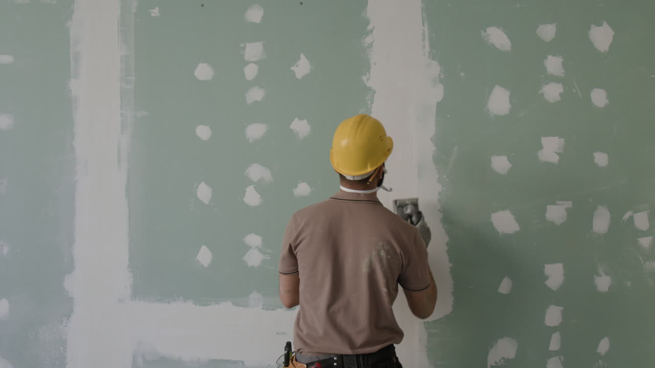 Construction worker smoothing drywall on a wall