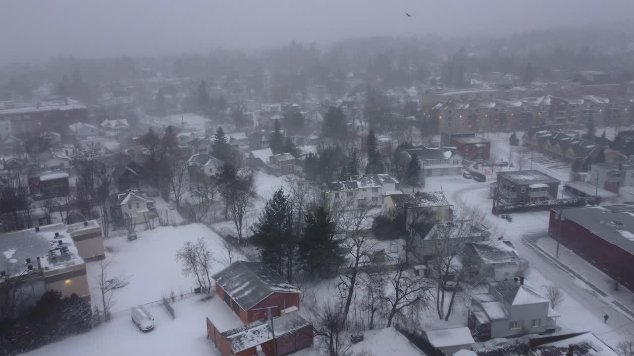 Aerial view of the city of Oxford, Québec, Canada, during a period of heavy snowfall. The image captures the blanket of white covering the residential areas, trees, and urban landscape in this winter.