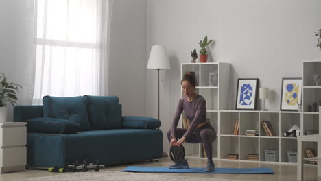 fitness at home young woman is crouching with weight in living room sporty and healthy lifestyle keeping fit during self-isolation wellness and sport activity