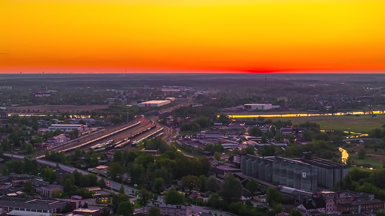 Aerial hyperlapse of sunrise over industrial cityscape with glowing horizon and railway tracks