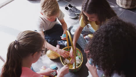 Gruppe-Von-Kindern,-Die-Zu-Hause-Auf-Dem-Boden-Sitzen-Und-Schokoladeneier-Essen,-Die-Sie-Bei-Der-Ostereiersuche-Gefunden-Haben