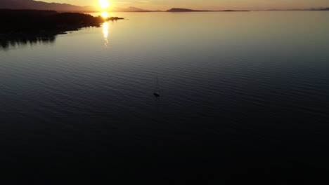 aerial view of sunset above ocean, isolated sailing boat and scenic coastline of vancouver island, british columbia, canada, static drone shot