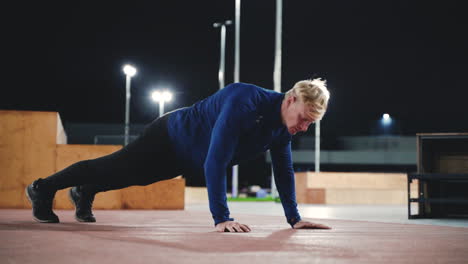 sportlicher blonder mann, der nachts im park liegestützübungen macht