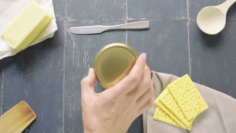 man's-hand-uncovers-pot-of-ghee-butter-on-table-with-cookies