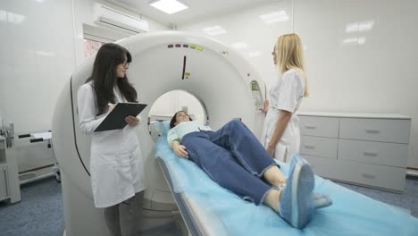 la paciente está siendo sometida a una tomografía computarizada o resonancia magnética bajo la supervisión de dos radiólogos calificados en una clínica médica moderna. la paciente está acostada en una mesa de tomografías computarizadas o mri, moviéndose fuera de la máquina