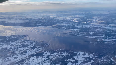 Flying-over-trondheim-fjord-with-stunning-reflection-of-the-clouds-on-the-water-in-a-snow-covered-arctic-landscape,-panning-right-to-left