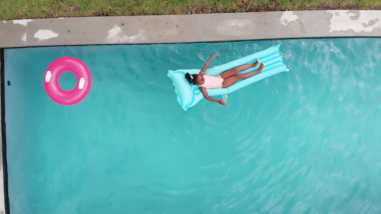 Overhead drone aerial shot of African American girl relaxing on blue pool float, copy space