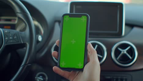 hombre de mano usando teléfono móvil chromakey con pantalla verde vacía en un coche moderno. maqueta de pantalla táctil. búsqueda en internet.