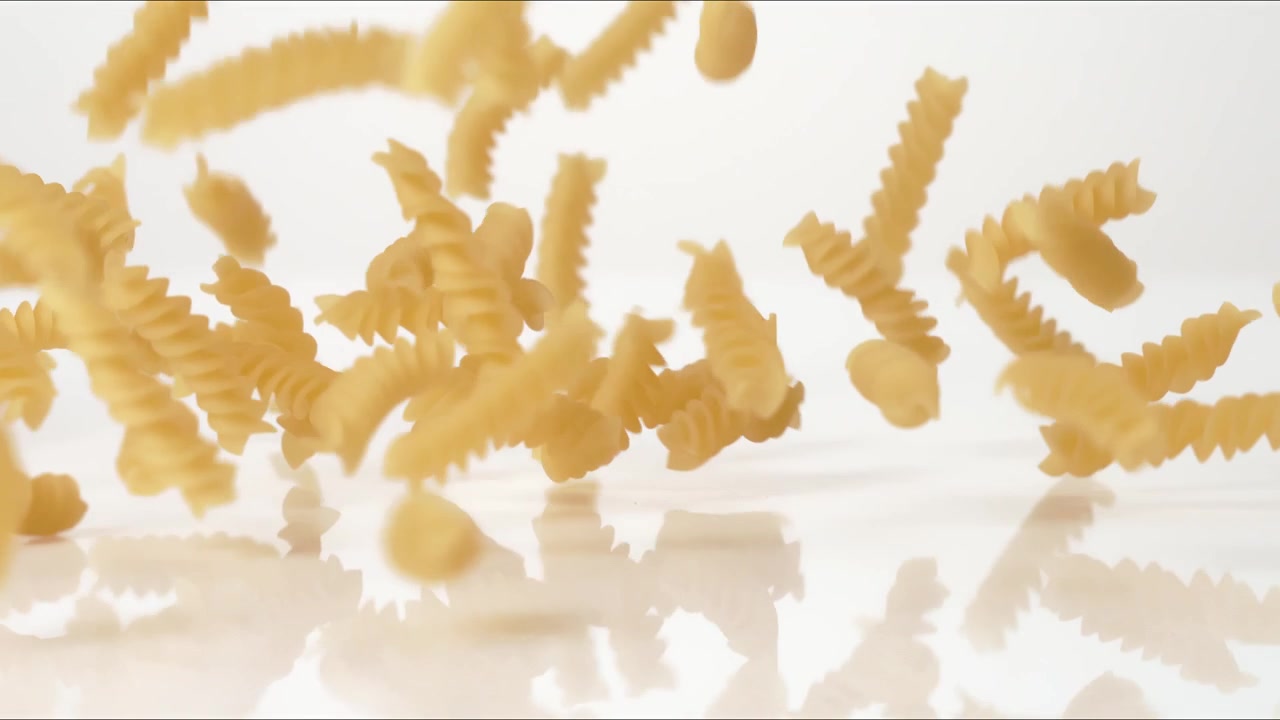 Dry uncooked Fusilli Rotini bouncing on a white tabletop in slow motion close up macro before settling.