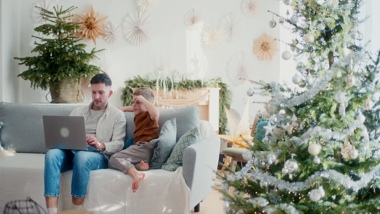 소년과 아빠가 소파에 앉아 온라인 크리스마스 쇼핑을 하고 있다