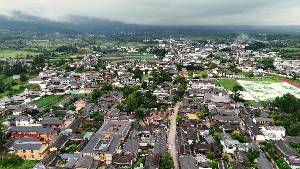 Baisha town rooftops and narrow streets with farmland and mountains near Fuguo Monastery Yunnan, aerial tracking along road