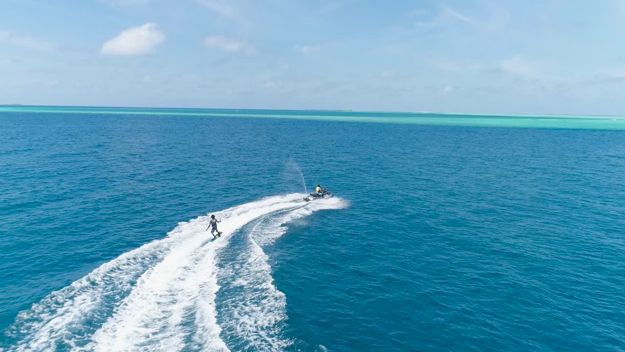 Drone tracking shot Over Man Riding A Jet Ski At Tropical Paradise Exotic Island with blue and turquoise ocean sea view. Adventure Concept for Tourist Attraction at Beach Vacation sport at Summer day