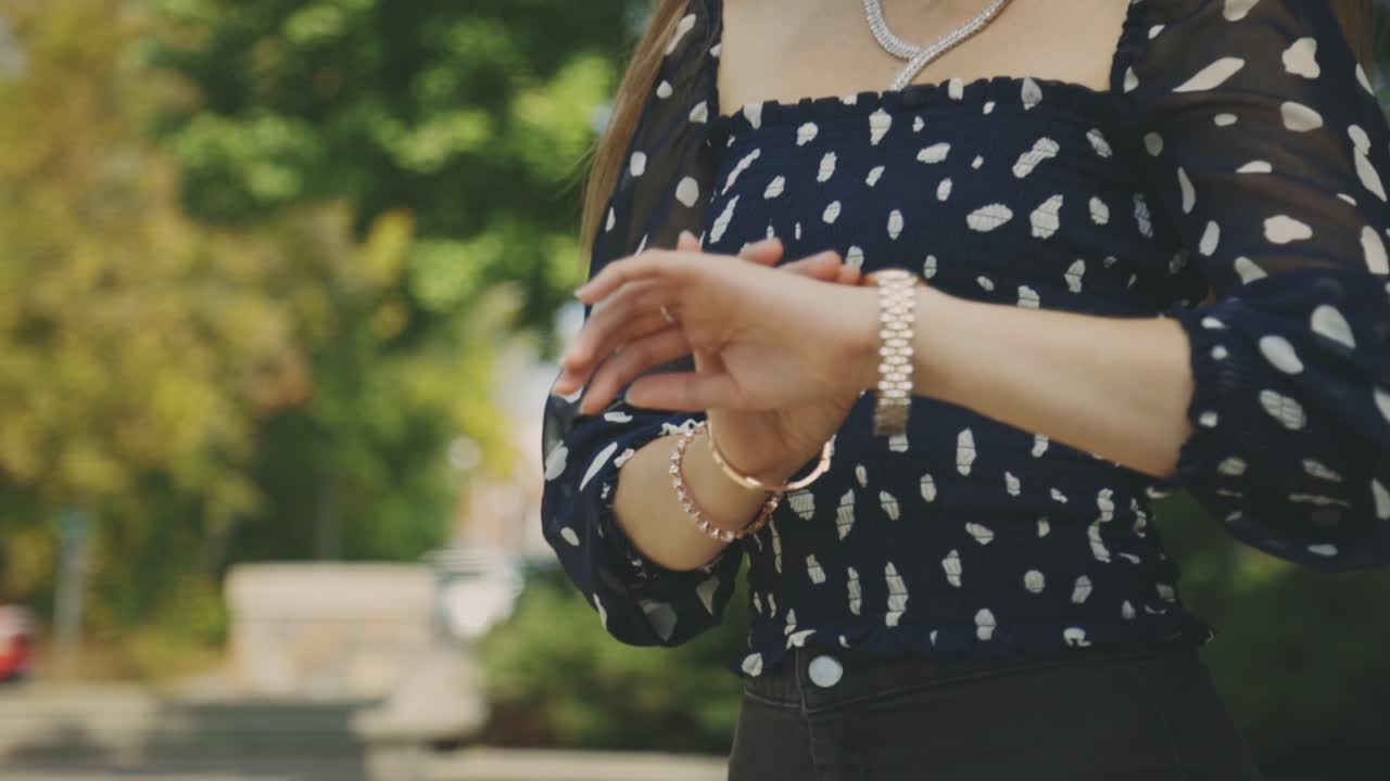 hermosa chica rubia con tops impresos revisando el tiempo en su reloj mientras espera su cita en el parque - tiro de primer plano medio a cámara lenta