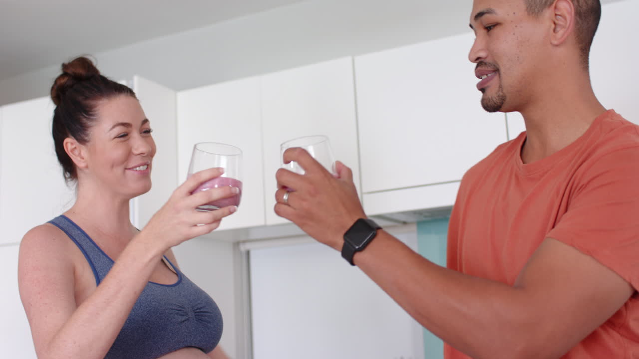 Pregnant woman and man toasting with smoothies in modern kitchen