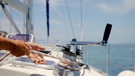 unwinding sailboat rope on winch, close up detail of sailman hands and sailing equipment