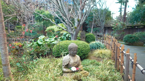 Un-Vídeo-Estabilizado-En-Cámara-Lenta-De-4k-Que-Muestra-Una-Hermosa-Estatua-De-Buda-Rodeada-De-Flores,-Plantas-Exuberantes-Y-árboles-En-Un-Jardín-De-Té-Japonés-En-San-Mateo,-California