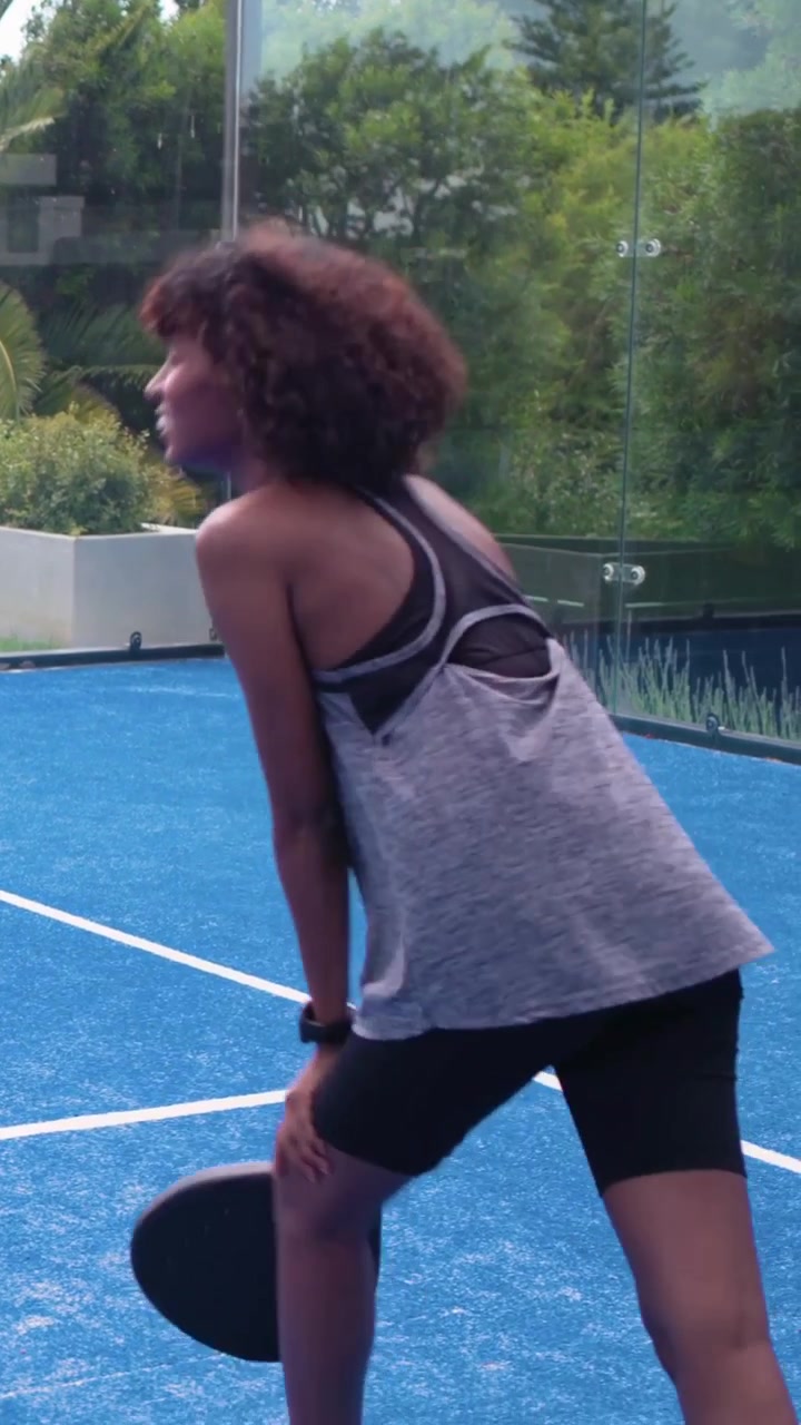 Vertical video: Tossing ball woman swinging black paddle practicing returns on garden court in kit
